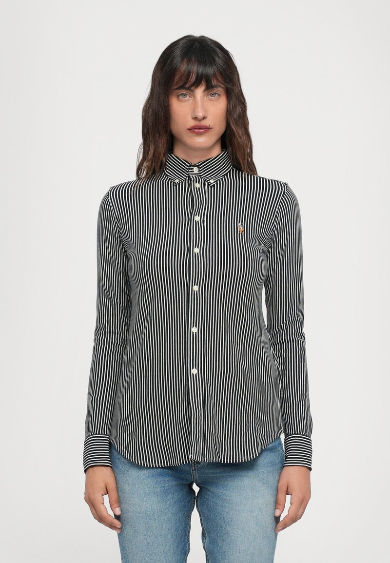 Chemise à rayures noires et blanches avec un col, dotée d'une fermeture à boutons sur le devant et de manches longues. Petit emblème sur la poitrine, texture en coton lisse.