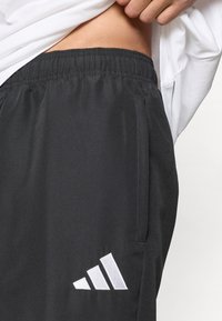 Μαύρο αθλητικό σορτς με ελαστική μέση, με λευκό λογότυπο Adidas κοντά στο τελείωμα και πλαϊνές τσέπες. Λείο ύφασμα.