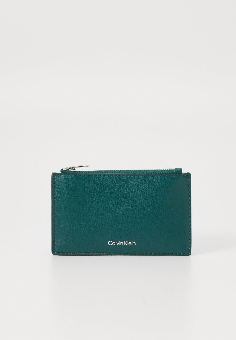 Teal leather cardholder with zip closure. Features a smooth texture and a white "Calvin Klein" logo on the front.
