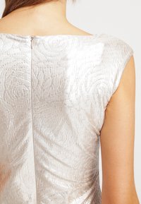 Zilverkleurige jurk met textuur en een bloemmotief, voorzien van een ritssluiting aan de achterkant en een brede halslijn, met een strak, aansluitend ontwerp.