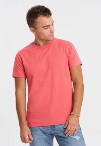 Koralfarvet t-shirt med korte ærmer lavet af bomuld, med en rund halsudskæring og en glat overflade, kombineret med lyseblå slidte jeans.