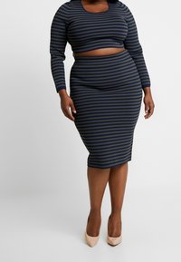 Striped two-piece outfit in dark blue and olive green. Long-sleeved cropped top with a round neckline, fitted pencil skirt, and beige heels.