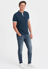 Námořnický polo s bílými akcenty, krátké rukávy a límec na knoflíky, kombinovaný s vybledlými modrými džíny a bílými teniskami.