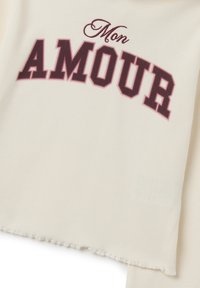 Top en tissu côtelé blanc avec le texte "Mon AMOUR" en bordeaux dans une police avec serif. L'ourlet est à bords bruts pour un look décontracté.