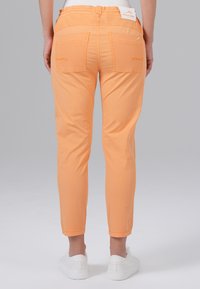 Oranje katoenen broek met een tapered fit, voorzien van twee achterzakken en een omslagzoom. Gedragen met witte sneakers.