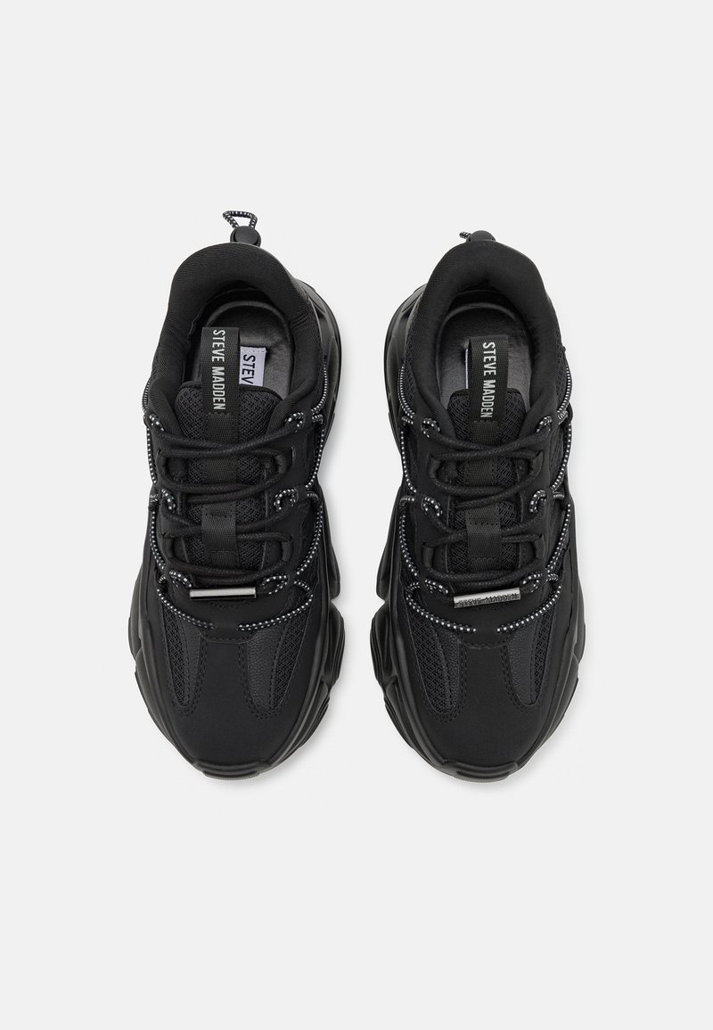 Scarpe da ginnastica nere realizzate con materiali tessili e sintetici, superficie strutturata, pannelli in rete, dettagli riflettenti e un sistema di allacciatura prominente.