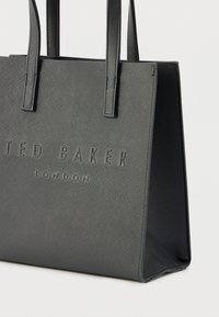 Μαύρη τσάντα ώμου από υλικό με υφή, με δύο λαβές και ανάγλυφο το όνομα της μάρκας "TED BAKER LONDON" στην πρόσοψη.