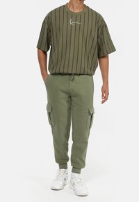 Olivgrön oversized T-shirt med svarta vertikala ränder och framåtriktat logotyp, ihopparad med matchande avsmalnande cargobyxor i sweatpants-stil med sidofickor.
