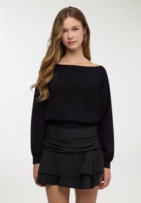 Maglione nero scollato con maniche lunghe abbinato a una minigonna nera con volant, caratterizzata da tessuto a strati e vita elastica.