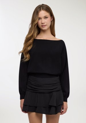 Maglione nero scollato con maniche lunghe abbinato a una minigonna nera con volant, caratterizzata da tessuto a strati e vita elastica.