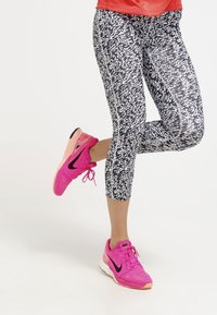 Černo-bílé legíny typu capri se vzorem spárované s jasně růžovými sportovními botami Nike, které mají černé detaily a síťovaný design.