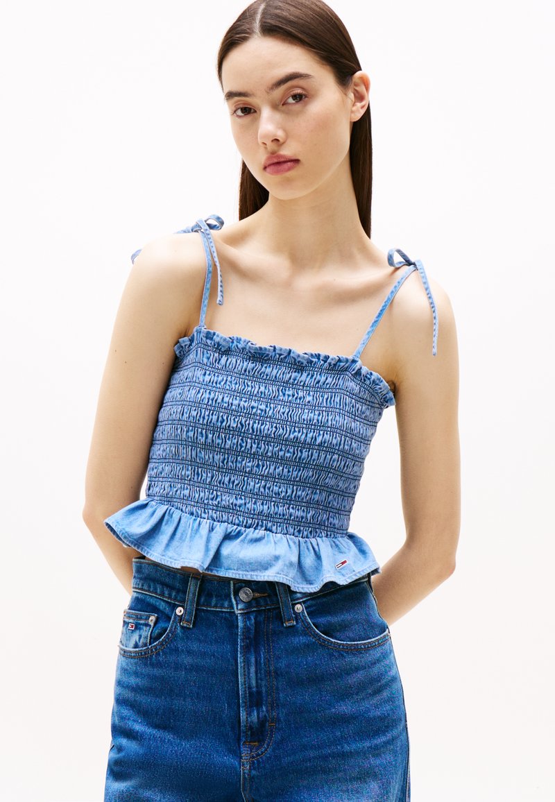Lys blå smocket kort topp med spaghettistrekk og volangkant. Sammen med høy midje denimshorts, som har et lite logotag.