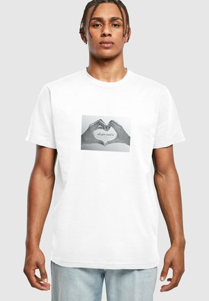White cotton t-shirt featuring a central graphic of two hands forming a heart shape with the text “all you need is” underneath.