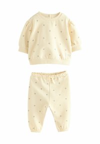 Cremfarbener Zweiteiler bestehend aus einem kurzärmeligen Top mit puffartigen Ärmeln und Herzmustern, kombiniert mit Hose mit elastischem Bund.