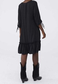 Svart klänning med volang nederkant, trekvartsärmar med knytdekorationer och en enkel rund halsringning. Bärs med svarta cowboystövlar.