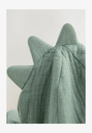 Zielony materiał o teksturowanym wykończeniu ma trójkątne kolce wzdłuż górnej krawędzi, tworząc zabawowy element wzorniczy.