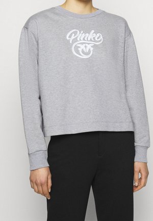 Osoba ubrana w jasnoszary sweatshirt z białym tekstem i logo "Pinko" z przodu, w połączeniu z czarnymi spodniami, pokazana od szyi do bioder.