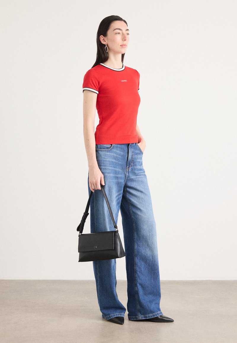 Camiseta de algodón roja con ribetes en blanco y negro, combinada con vaqueros de pierna ancha de color azul y un pequeño bolso negro con un logo.