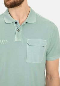Lichtgroen poloshirt van gestructureerde stof, met een knoopsluiting kraag, geborduurd logo en een borstzak met een contrasterende klep.