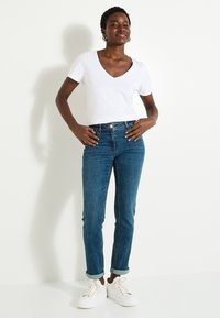 Camiseta blanca de manga corta y escote en V combinada con jeans oscuros ajustados con dobladillo enrollado y zapatillas de plataforma blancas. Diseño simple y colores clásicos.