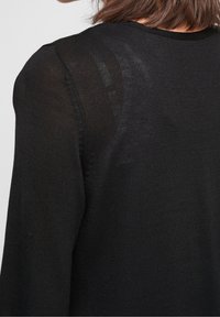 Black knit sweater featuring a textured pattern, round neckline, and long sleeves, showcasing a fitted design and subtle sheen.