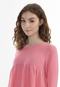 Top a maniche lunghe rosa con motivo a diamante testurizzato e vestibilità ampia. Collo rotondo, dettagli arricciati e tessuto morbido.