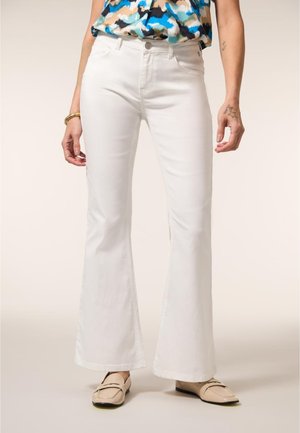 Witte, hooggetailleerde wijde jeans gedragen met beige loafers en een mouwloos topje met een blauw, zwart en beige patroon.