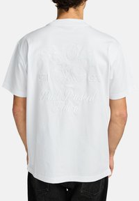 Weißes Baumwoll-T-Shirt mit erhabenem, gesticktem Text und Globen-Design auf der Rückseite. Kurze Ärmel, lockere Passform, keine sichtbaren Muster oder Akzente.