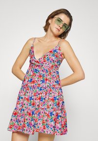 Vestido de verão floral em tons de rosa, vermelho e azul, com um decote em V profundo, alças finas e saia em camadas. Tecido leve e respirável.