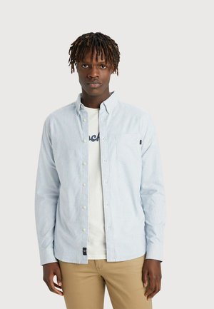Lichtblauwe en witte gestreepte button-up shirt van katoen, lange mouwen, voorzak, gedragen over een wit T-shirt, gecombineerd met beige broek.