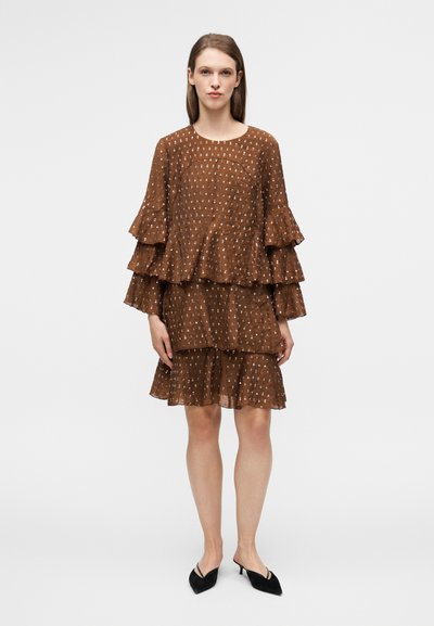 Robe marron à volants superposés en trois couches, ornée de petits pois blancs. Fabriquée en tissu léger, avec un col rond et des manches longues.