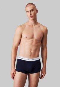 Navyblauwe katoenen boxershorts met een witte merkband, met een strakke pasvorm en een soepele textuur, weergegeven op een neutrale grijze achtergrond.
