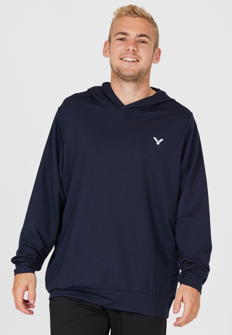 Marinblå långärmad hoodie gjord av ett slätt tyg, med en framficka, dragsko i huven och en liten logotyp på bröstet.