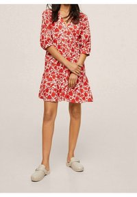 Robe à imprimé floral rouge avec des manches courtes bouffantes, décolleté en V et jupe à volants. Associée à des sabots slip-on gris clair avec des accents cloutés.
