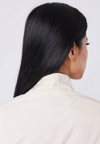 Lichtbeige jas met een hoge kraag, voorzien van een subtiele blauwe sterdetail op de achterkant. Glad fabric, aansluitend ontwerp.