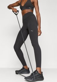 Czarny sportowy biustonosz i legginsy wykonane z elastycznego materiału, z dopasowanym krojem i subtelnymi akcentami z logo. Czarne buty sportowe z teksturowanym wzorem.