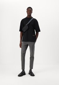 Sort oversized t-shirt med guldtekst, grå skræddersyede bukser, sort crossover taske og sorte sko med kraftige såler. Minimalistisk design.