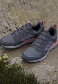 Gray athletic shoes with textured mesh upper, grey rubber sole, and orange accents, featuring laces and a reinforced heel.