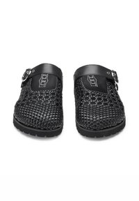 Zoccoli neri intrecciati con tomaia texturizzata, punta rotonda e cinturino regolabile con hardware metallico. La suola in gomma offre aderenza e durabilità.