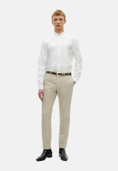 Witte blouse met lange mouwen, een staande kraag en gestructureerde voorpanden, gecombineerd met lichtbeige op maat gemaakte broek en zwarte enkellaarsjes.