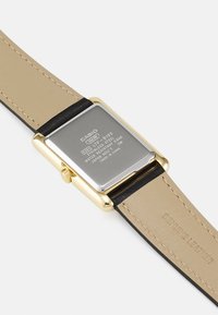 Montre rectangulaire Casio avec un boîtier en acier inoxydable doré, un bracelet en cuir véritable beige et des accents noirs. Comprend des détails de résistance à l'eau.
