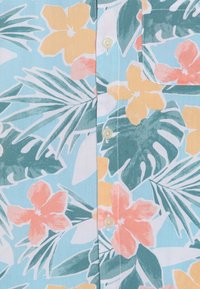 Korte mouwen overhemd van lichtblauwe stof met een bloemenpatroon met gele, roze en turquoise bloemen en groene bladeren. Voorzien van knoopsluiting.