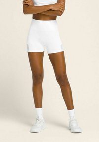 Pantaloni atletici bianchi con un alto elastico in vita e pannelli laterali in rete, abbinati a scarpe da ginnastica e calze bianche, su uno sfondo chiaro.