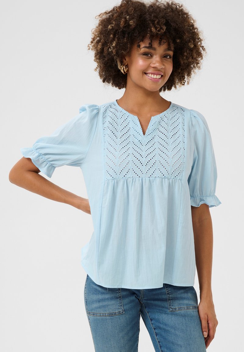 Világoskék blúz puffos ujjakkal, V-nyakkal és bonyolult hímzett részletekkel a mellrészen. Puha anyag, laza szabással.