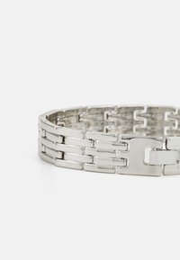 Bracelet en métal argenté avec des maillons entrelacés, des formes rectangulaires et un fini poli, doté d'un fermoir sécurisé.