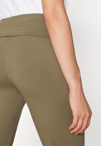 Olivenfargede leggings med høy liv, laget av et elastisk stoff som følger kroppens former, med en glatt tekstur.