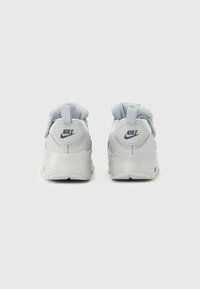 Fehér Nike tornacipőpár hátulnézetből, párnázott szegélyekkel, húzófülekkel és látható Nike logókkal a sarokrészen.