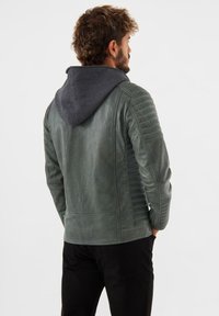 Giacca di pelle verde con cappuccio grigio, pannelli sulle spalle texturizzati e design aderente. La vista posteriore mostra dettagli lisci e a coste.