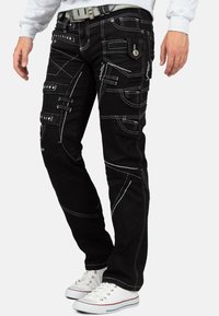 Pantaloni cargo in denim nero con multiple tasche, dettagli in cuciture bianche e vestibilità dritta. Abbinati a sneaker bianche, che mostrano uno stile casual.