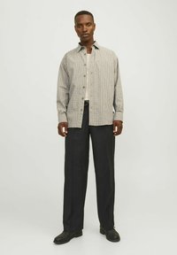 Chemise à carreaux en gris clair et marine avec des boutons, portée par-dessus un débardeur blanc, associée à un pantalon sombre et des chaussures noires.
